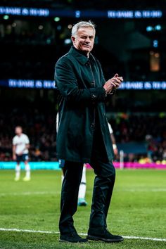 an older man standing on top of a soccer field with his hands in his pockets