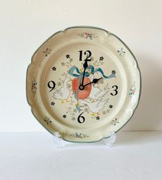 a clock that is sitting on top of a table next to a white wall behind it