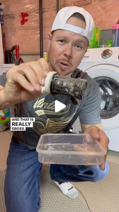 a man is holding something in front of his face while sitting on the floor next to a washer