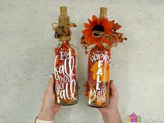 someone holding two bottles with fall decorations on them