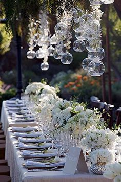 a long table with white flowers and clear bubbles hanging from it's centerpieces