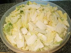 a bowl filled with lettuce and onions on top of a counter next to a knife