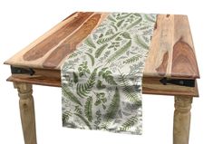 a wooden table topped with a white and green leafy table runner on top of it