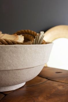 a white bowl filled with rope on top of a wooden table next to a banana