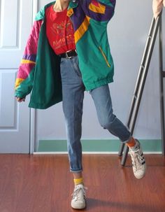 a woman standing on top of a hard wood floor next to a ladder wearing a green jacket