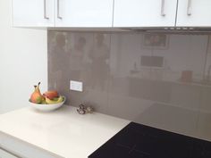 a bowl of fruit sitting on top of a counter next to white cupboards in a kitchen