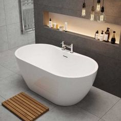 a white bath tub sitting in a bathroom next to a wooden mat and bottles on the wall