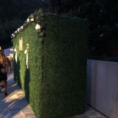 people walking down a sidewalk next to a tall green wall covered in plants and flowers