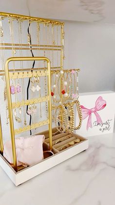 a white box with gold jewelry in it and a pink pillow on the side next to it