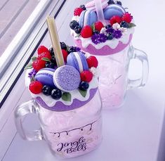 two glass mugs filled with colorful fruit and cake decorations on top of a window sill