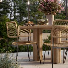 a table with chairs and a vase filled with flowers on top of it next to some plants