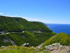 a winding road in the middle of a green mountain with water and trees on both sides