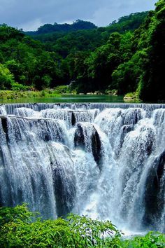 a large waterfall with water cascading down it's sides and trees in the background