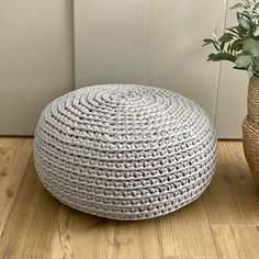 a white round ottoman sitting on top of a wooden floor next to a potted plant