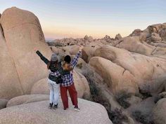 two people standing on top of rocks with their arms in the air and one person raising their hands