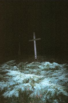 a wooden cross sitting in the middle of a field at night with snow on it