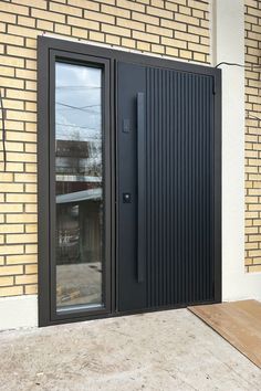 a black door is open on the side of a brick building with glass doors and wood flooring