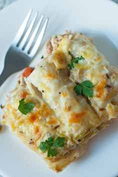 a white plate topped with lasagna covered in cheese and parsley next to a fork