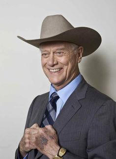 an older man in a suit and tie wearing a cowboy hat smiles at the camera