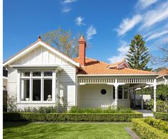 a white house with a red roof surrounded by greenery and shrubs on a sunny day