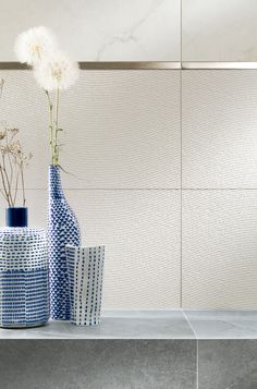 three vases with flowers in them sitting on a table next to a wall and tile