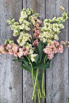 a bunch of pink and white flowers sitting on top of a wooden table next to a fence