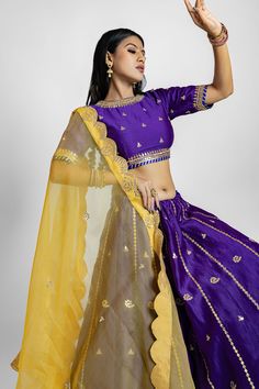 About This Product Radiating regal charm, this masterpiece combines the richness of pure Chanderi silk and the delicate allure of pure organza fabric. The lehenga's stunning purple and yellow color palette creates a vibrant and captivating aesthetic, perfect for grand celebrations. The intricate gota patti handwork adds a touch of traditional artistry, meticulously woven into every inch of the fabric. The lehenga skirt flows gracefully, offering a magnificent drape that complements the wearer's movements. The matching choli, adorned with the same intricate gota patti work, provides a cohesive and sophisticated look. Completing the ensemble is a delicate dupatta in organza, adorned with gota patti borders, adding a final touch of grace and refinement. Product Highlights for A Handcrafted Pu Purple Raw Silk Sets For Eid, Purple Anarkali Set In Raw Silk, Purple Anarkali Raw Silk Set, Anarkali Purple Raw Silk Set, Purple Chanderi Bollywood Sharara, Bollywood Style Purple Chanderi Sharara, Purple Raw Silk Sets For Navratri, Purple Raw Silk Sets With Zari Work, Purple Art Silk Sharara With Dupatta