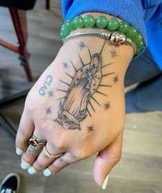 a woman's hand with a tattoo on it and a green beaded bracelet