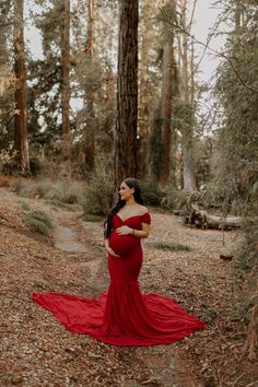 a pregnant woman in a red dress standing in the woods