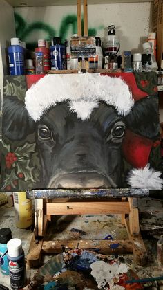 a painting of a cow wearing a santa hat on it's head in a studio