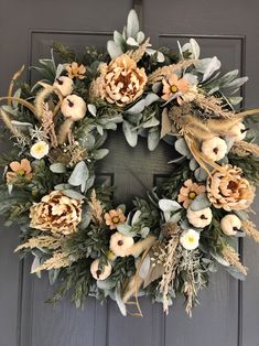 a wreath is hanging on the door with flowers and leaves around it in front of a gray door