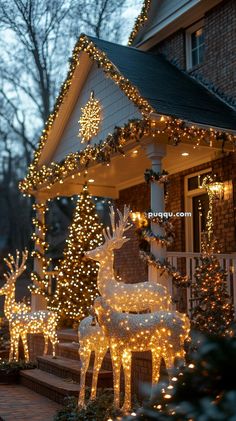 christmas lights decorate the front porch of a house with deer statues and trees in front