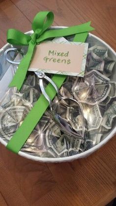 a bowl filled with lots of money sitting on top of a wooden table next to a green ribbon