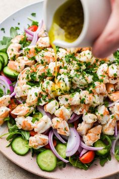 someone pouring dressing onto a salad with shrimp and cucumbers