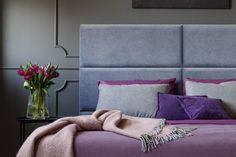 a purple and grey bed with pink flowers in a vase on the nightstand next to it