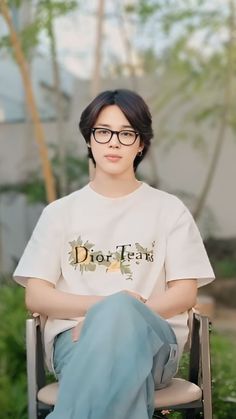 a woman sitting in a chair with her legs crossed, wearing glasses and a diorma t - shirt