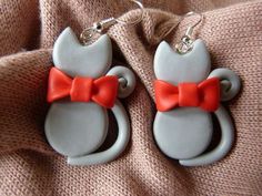 two cat shaped earrings with red bows on them