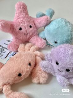 four different colored stuffed animals are on a white tablecloth, one is pink, the other is blue