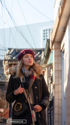 a woman wearing a hat and scarf standing in the middle of an alleyway with her hand on her hip