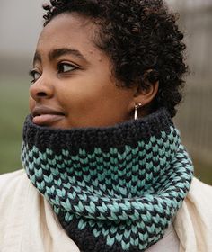 a woman with curly hair wearing a knitted cowgirl neck scarf in green and black