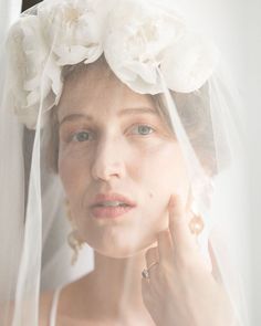 a woman wearing a veil and flowers in her hair is looking at the camera while she holds her hand up to her face