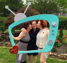 three women are posing in front of a tv with the word love written on it