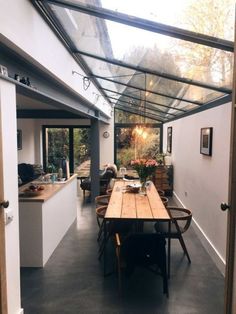 a long table sitting under a glass roof in a kitchen next to an open door