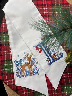 two christmas napkins on top of a table with a pine tree in the background