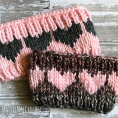 two pink and black knitted wrist warmers sitting on top of a wooden table