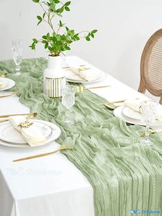 the table is set with plates, silverware and a green cloth draped over it