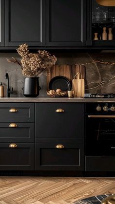 a kitchen with black cabinets and gold handles on the countertop, along with a vase filled with flowers