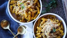 two white bowls filled with pasta and parmesan cheese on top of a blue towel