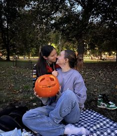 a woman and child sitting on a blanket with an orange pumpkin