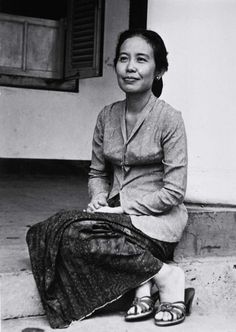 an old photo of a woman sitting on the steps in front of a building with her feet crossed